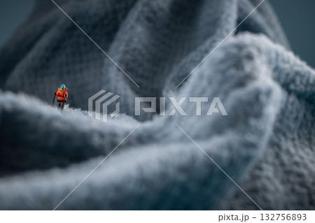 A miniature mountain climber figurine on a fuzzy fleece lining resembling a snow-covered surface, with a blurred background of a mountain or ice wall A miniature mountain climber figurine on a fuzzy fleece lining resembling a snow-covered surface, with a blurred background of a mountain or ice wall 132756893