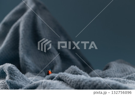 A miniature mountain climber figurine on a fuzzy fleece lining resembling a snow-covered surface, with a blurred background of a mountain or ice wall A miniature mountain climber figurine on a fuzzy fleece lining resembling a snow-covered surface, with a blurred background of a mountain or ice wall 132756896