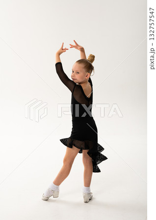 Little girl in black latin dance dress performing graceful pose with cochlear implant. Overcoming hearing loss through movement, inclusion, and confidence in art and rhythmic self-expression. 132757547
