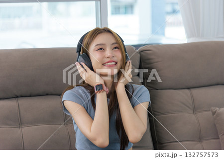 Young woman happy at home, people engaging in relaxing activity, enjoying music through headphones on comfortable sofa, joyful expression, modern lifestyle leisure time indoors. Young woman happy at home, people engaging in relaxing activity, enjoying music through headphones on comfortable sofa, joyful expression, modern lifestyle leisure time indoors. 132757573