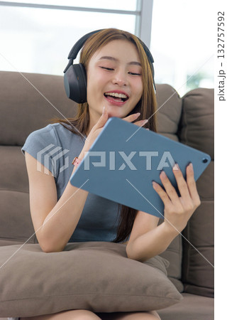 Young happy woman enjoying home activity, people find relaxation on comfy sofa, wearing modern headphones, laughing joyfully while watching content on digital tablet for leisure. Young happy woman enjoying home activity, people find relaxation on comfy sofa, wearing modern headphones, laughing joyfully while watching content on digital tablet for leisure. 132757592