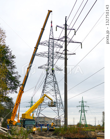 Workers installing high-voltage power line tower using cranes and lifts at construction site Workers installing high-voltage power line tower using cranes and lifts at construction site 132758143