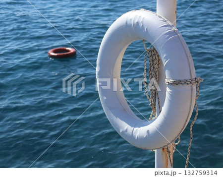 White Lifebuoy On Pole Over Blue Water With Red Buoy In Background - Nautical Safety Image 132759314