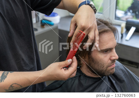 A hairdresser uses scissors and a red comb to give a haircut to a male client A hairdresser uses scissors and a red comb to give a haircut to a male client 132760063
