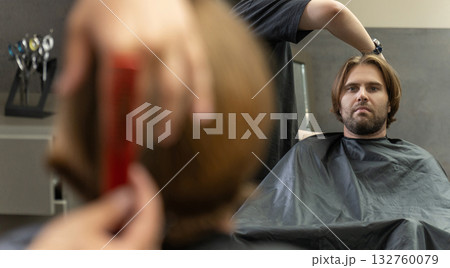 A hairdresser cuts a male client's long brown hair in a barbershop A hairdresser cuts a male client's long brown hair in a barbershop 132760079