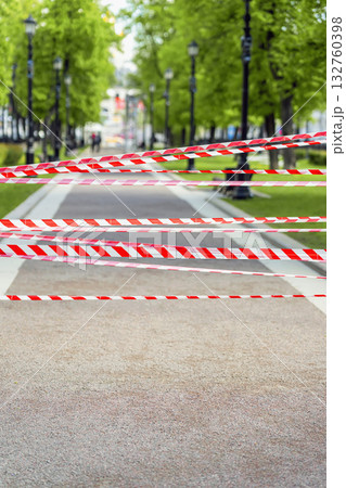Urban park walkway blocked with red and white warning tape restricting access to public area. Concept of closure, restriction, and emergency safety in city environment 132760398
