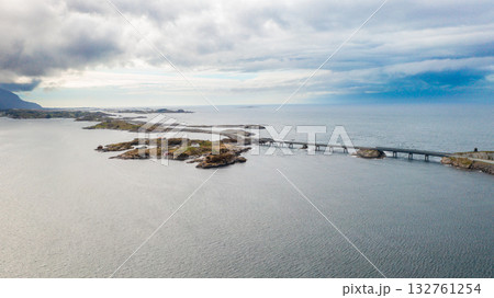 Magnificent stretch of Atlantic ocean road with long bridge gracefully spanning deep blue waters. Rough waves crash near rugged coastline in Norway 132761254