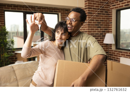 Diverse couple presenting house keys and carrying cardboard box during relocation. Boyfriend and girlfriend celebrate becoming homeowners and new beginnings in modern apartment on moving day. Diverse couple presenting house keys and carrying cardboard box during relocation. Boyfriend and girlfriend celebrate becoming homeowners and new beginnings in modern apartment on moving day. 132761632