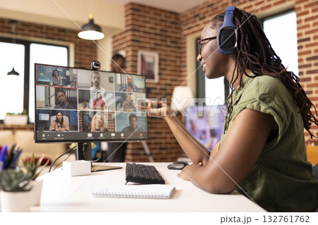 Black female manager uses headphones and computer in communicating with colleagues during virtual meeting. Self employed woman virtually presenting startup project with potential clients on video call 132761762