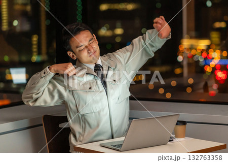 夜、パソコンの前でストレッチをする作業服の男性 132763358