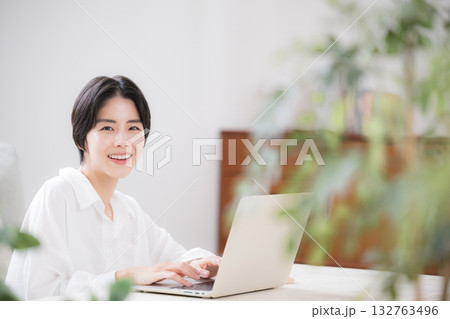 緑のあるリビングでパソコンを使う女性　カメラ目線 132763496