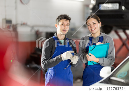 Car service manager discusses car repair problems with mechanic. He takes notes on paper 132763724