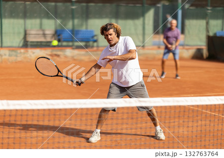 Sporty two men during doubles match on tennis court. Active sportsman hitting tennis ball with racket Sporty two men during doubles match on tennis court. Active sportsman hitting tennis ball with racket 132763764