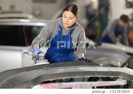 Young woman auto mechanic polishes body parts by car buffer polisher machine tool 132763883