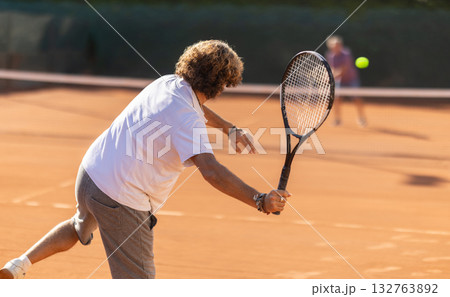 Back view of active male player hitting ball with racket on tennis court on blurred background of opponents 132763892