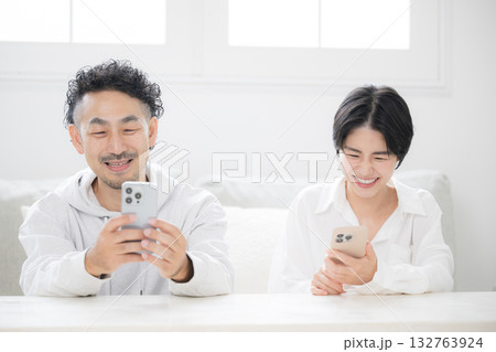 リビングでスマホを見るミドルの笑顔の夫婦やカップル リビングでスマホを見るミドルの笑顔の夫婦やカップル 132763924