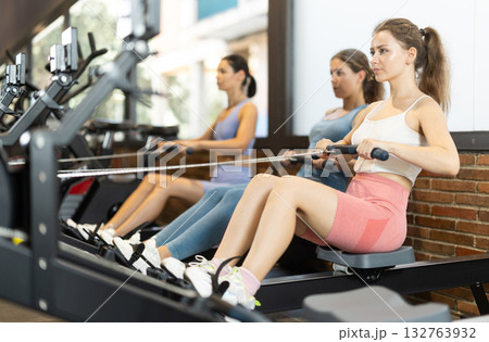 Women are engaged on a rowing machine Women are engaged on a rowing machine 132763932