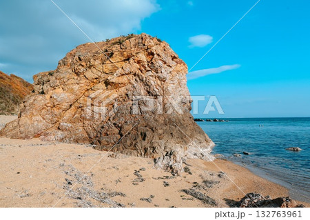Rocky cliff on a sandy beach at Shamora Bay, Cape Zelyony, Vladivostok. Clear blue sea and bright sky create a calm summer coastal background. Rocky cliff on a sandy beach at Shamora Bay, Cape Zelyony, Vladivostok. Clear blue sea and bright sky create a calm summer coastal background. 132763961