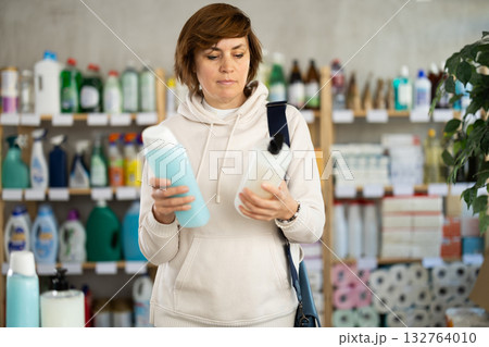 Woman buyer chooses shampoo or shower gel in household goods department of supermarket 132764010