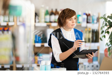 Woman seller, with tablet in hands, make inventory in store. 132764393