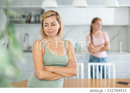 Upset woman standing in home kitchen against background of dissatisfied teenage daughter Upset woman standing in home kitchen against background of dissatisfied teenage daughter 132764415