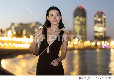 Woman walks by waters edge Mediterranean Sea, hotel skyscraper Arts in background 132764526