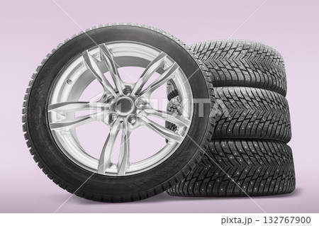 A tire shop showcases a set of four winter tires stacked beside an alloy wheel. These studded tires are designed for improved traction in winter conditions, perfect for safe driving. A tire shop showcases a set of four winter tires stacked beside an alloy wheel. These studded tires are designed for improved traction in winter conditions, perfect for safe driving. 132767900