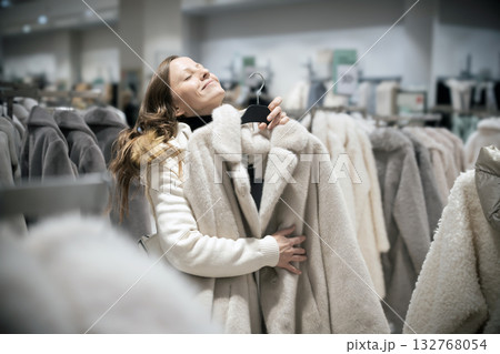A beautiful 30-35-year-old woman dreamily hugs a new winter fur coat in a fashion boutique store. She dreams of giving a gift or buying a new fashionable fur coat or winter coat. 132768054