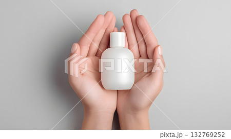 Hands holding a white cosmetic bottle on a soft gray background for beauty product display Hands holding a white cosmetic bottle on a soft gray background for beauty product display 132769252