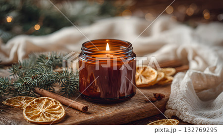 Scented candle with warm glow surrounded by dried fruits and festive greenery elements Scented candle with warm glow surrounded by dried fruits and festive greenery elements 132769295