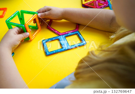 A colorful collection of magnetic geometric shapes is being transformed by a child into creative three-dimensional designs and constructions. 132769647