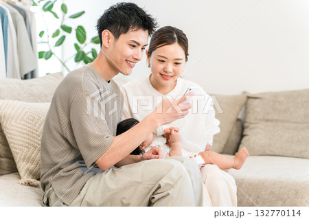 ソファーに座りスマホを見る子育て世代の夫婦（アプリ,オンライン申請,子育て支援） 132770114