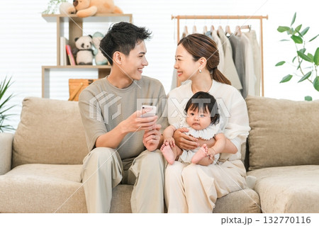 ソファーに座りスマホを見る子育て世代の夫婦（アプリ,オンライン申請,子育て支援） 132770116
