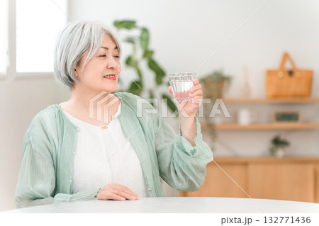 自宅のリビングで水,ミネラルウォーターを飲むグレイヘアーのシニア女性 132771436