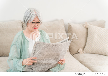 自宅のソファーで新聞を読むグレイヘアーのシニア女性 自宅のソファーで新聞を読むグレイヘアーのシニア女性 132771447