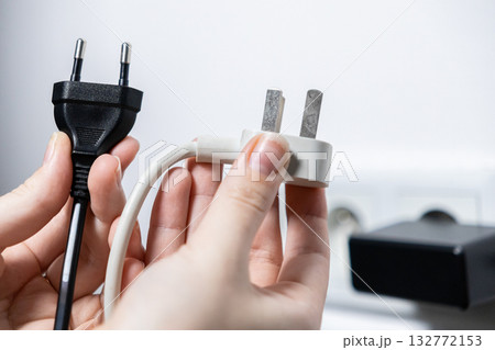 Hands comparing black European and white British electrical plugs, illustrating global power compatibility standards for international travel and device connectivity solutions Hands comparing black European and white British electrical plugs, illustrating global power compatibility standards for international travel and device connectivity solutions 132772153