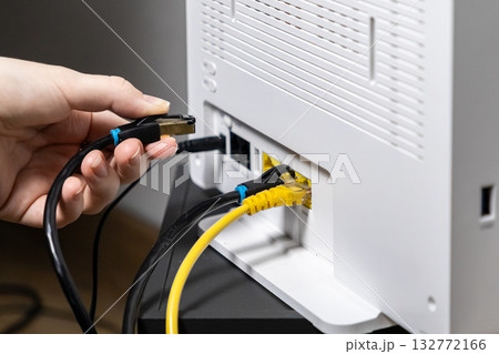 Person's hand connecting a black Ethernet cable into a white wireless internet router, symbolizing network setup, reliable broadband, and home technology Person's hand connecting a black Ethernet cable into a white wireless internet router, symbolizing network setup, reliable broadband, and home technology 132772166