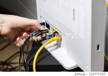 Human hand plugging a black Ethernet cable into a white internet router, establishing a secure network connection for modern digital technology setup 132772167
