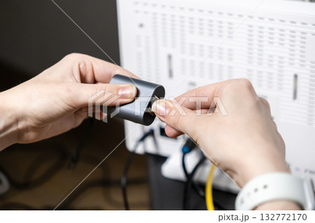 Person's hands meticulously connect an Ethernet LAN cable into a sleek gray adapter, ensuring stable internet for digital work and home office connectivity Person's hands meticulously connect an Ethernet LAN cable into a sleek gray adapter, ensuring stable internet for digital work and home office connectivity 132772170