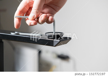 Human hand precisely adjusting a furniture leg's leveling foot with a hex key, representing home assembly and DIY repair Human hand precisely adjusting a furniture leg's leveling foot with a hex key, representing home assembly and DIY repair 132772197