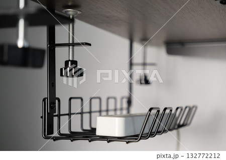 Durable black metal wire cable management tray securely clamped under dark wooden office desk, neatly organizing essential power strip for optimal productive home workspace Durable black metal wire cable management tray securely clamped under dark wooden office desk, neatly organizing essential power strip for optimal productive home workspace 132772212