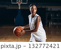African American teen girl in white sportswear with a basketball ball on the court indoors, movement. 132772421