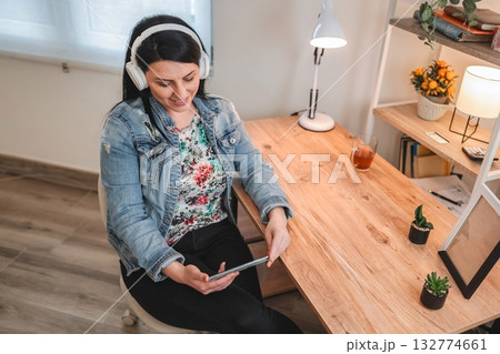 Freelancer working from home listening music with headphones and holding tablet Freelancer working from home listening music with headphones and holding tablet 132774661