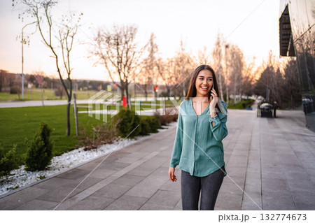 Young businesswoman walking and talking on smartphone in a park near office buildings 132774673