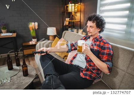Young man relaxing on sofa, drinking beer and watching tv 132774707