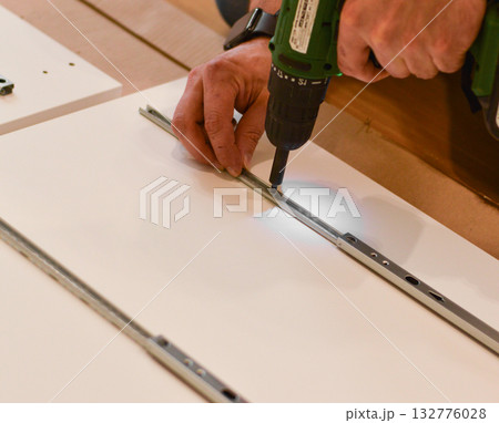 Furniture assembly. A worker is screwing a hinge into a wooden closet door. Adjustment of fittings, door hinges. The concept of installing furniture, home renovation. 132776028
