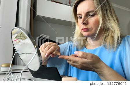 A young woman is intently applying her makeup while looking into a mirror, carefully perfecting her appearance in the reflection before heading out. 132776042