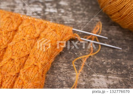 Cozy knitted socks with yarn ball and knitting needles. Orange wool socks on wooden background. Cozy autumn colours. Knitting pattern close up. Knitting hobby. Knitwear concept. Needlework background. 132776070