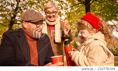 Father laughing as daughter pours tea under grandmother smile Father laughing as daughter pours tea under grandmother smile 132776104