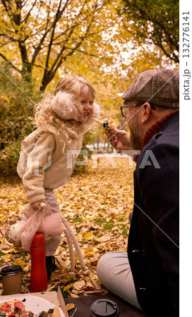 Father feeding smiling daughter pizza during autumn picnic Father feeding smiling daughter pizza during autumn picnic 132776141